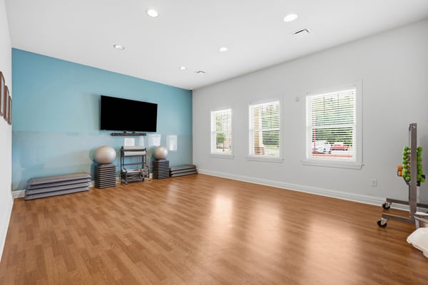 Spacious multi-purpose room with ample natural light, featuring a mounted TV and versatile flooring for various activities.
