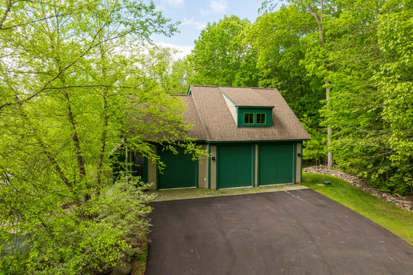 This property features a spacious garage surrounded by lush greenery, providing ample storage and outdoor appeal with 3 levels, first and second levels heated and 3 garage bays.