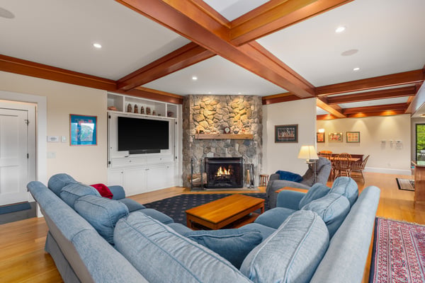 Cozy living area featuring a stone fireplace, wooden beams, and ample natural light for gatherings.