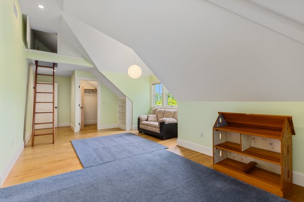 Bright, versatile attic space featuring a cozy sitting area, ladder access, and ample natural light.