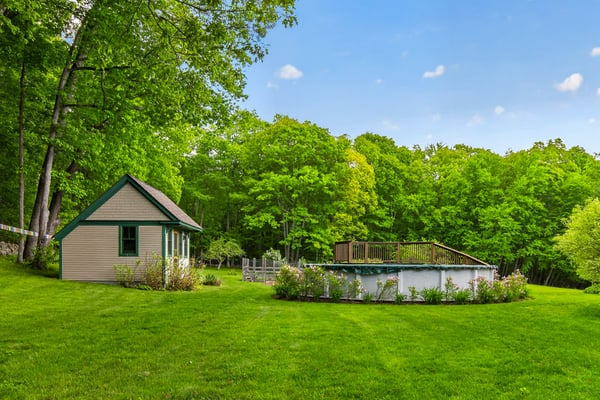 This property features a spacious backyard with a pool, surrounded by lush greenery and a quaint storage shed.