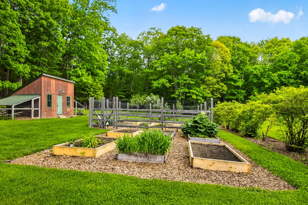 Discover a beautifully landscaped outdoor space featuring raised garden beds and a spacious shed amid lush greenery.