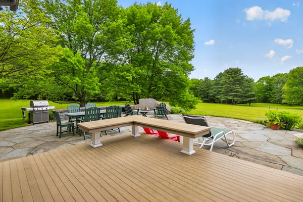 Spacious outdoor patio with seating and grilling area, surrounded by lush greenery and open, inviting space.