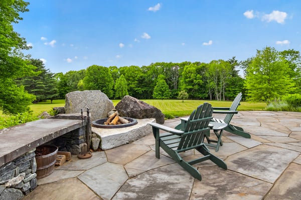 Discover a spacious outdoor retreat featuring a stone fire pit surrounded by lush greenery and tranquil views.
