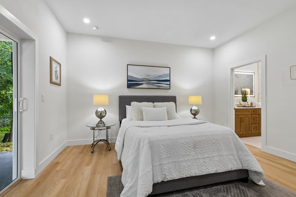 Bright and airy bedroom featuring modern decor, dual bedside lamps, and direct access to outdoor greenery.