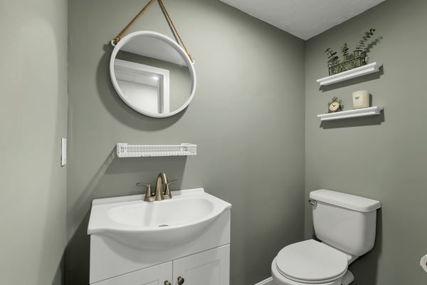 Modern bathroom featuring a sleek vanity, round mirror, and practical shelving for added storage.