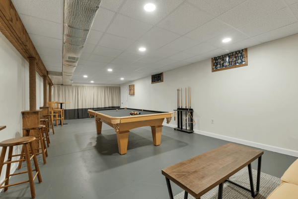 Spacious recreational room featuring a billiards table, bar seating, and ample natural light from large windows.