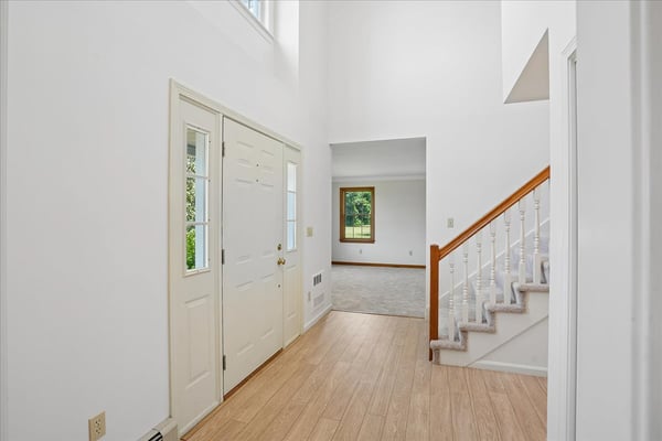 Bright and inviting entryway featuring a two-story ceiling, staircase, and views of the spacious living area.