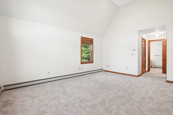 Spacious room with vaulted ceiling, large windows, and neutral carpeting, ready for your personal touch.