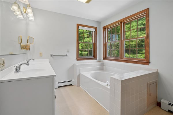 Spacious bathroom featuring natural light, a large tub, and picturesque views through multiple windows.