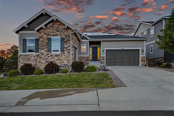 Modern home with stone accents, solar panels, and a spacious lawn, ideal for comfortable living.