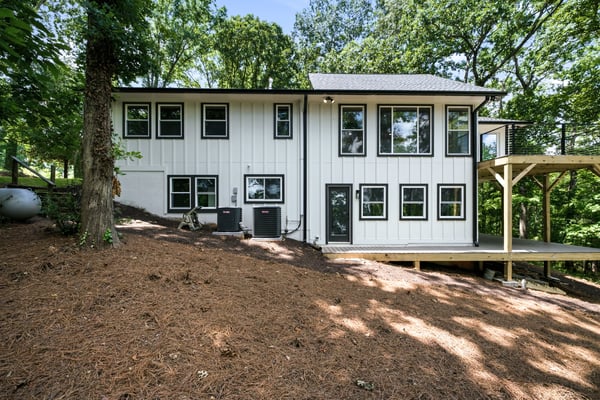 Modern home surrounded by lush greenery, featuring expansive windows and a spacious deck for outdoor living.