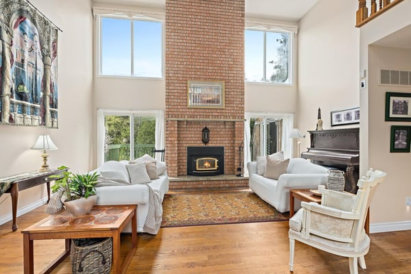 Bright, inviting living space features a striking brick fireplace and large windows, perfect for relaxed gatherings.