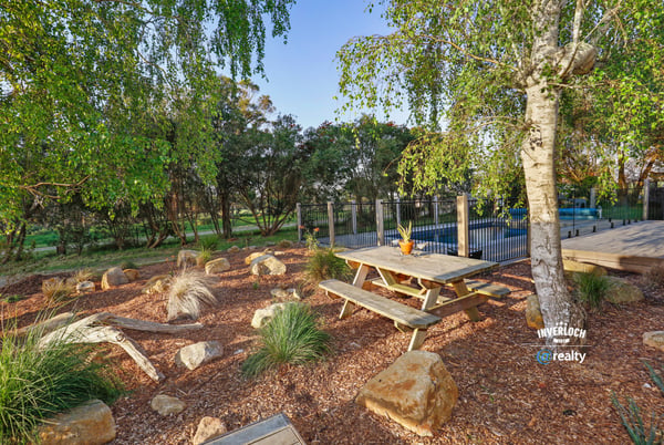 This outdoor space features a picnic area surrounded by native landscaping and a pool in the background.