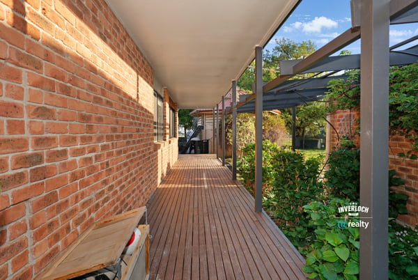 Inviting walkway lined with brick and greenery, leading to a secluded outdoor living space.