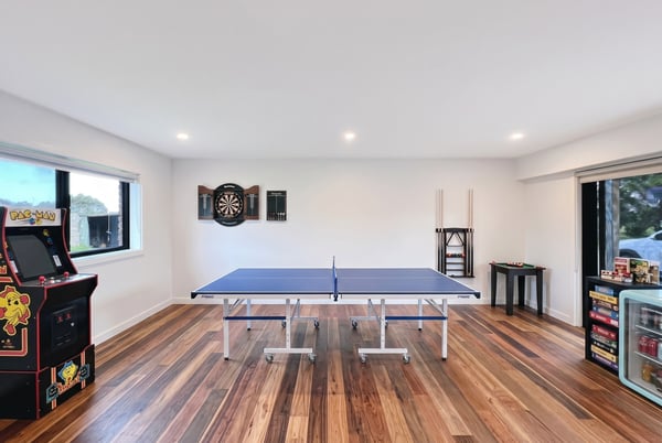 Bright recreational space featuring a ping pong table, arcade machine, and dartboard for entertainment.