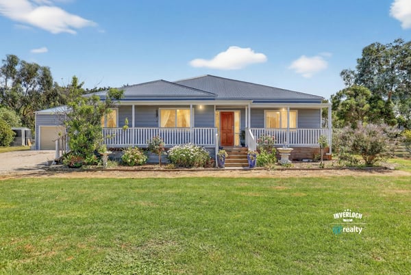 Spacious home surrounded by landscaped gardens, featuring a welcoming porch and ample outdoor space for relaxation.