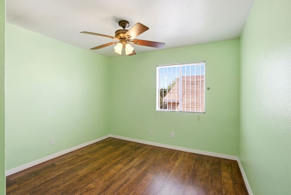 Bright, airy room with a ceiling fan, large window, and fresh paint, ideal for versatile use.