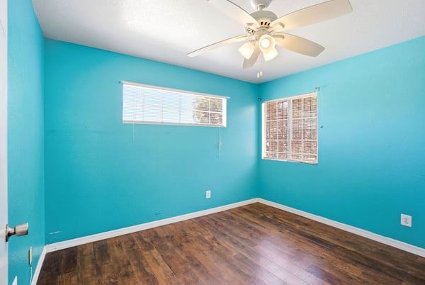 Brightly painted room with ample natural light, featuring a ceiling fan and modern wood flooring.