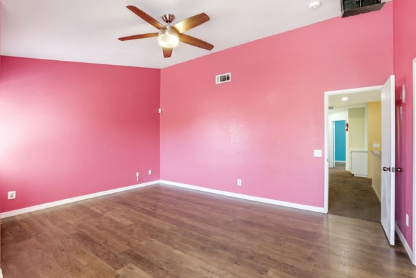 Bright, vibrant room with a unique pink accent wall and modern ceiling fan, perfect for personalization.