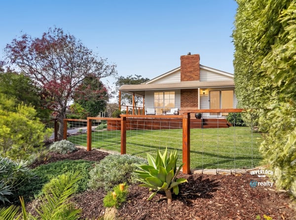 This inviting home features a spacious yard surrounded by vibrant landscaping and a welcoming front porch.