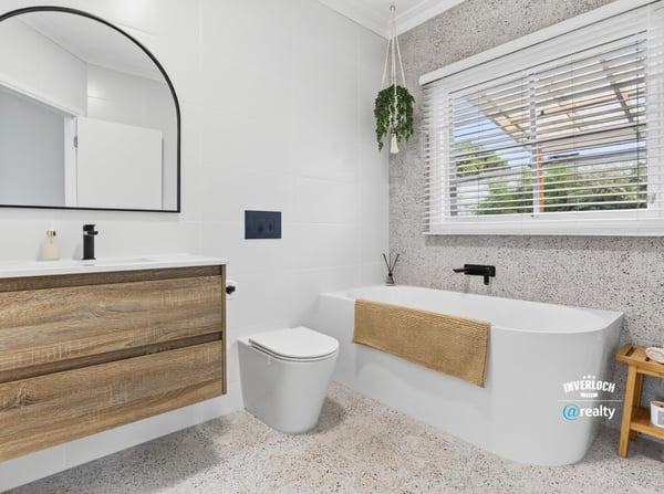 Modern bathroom featuring a freestanding tub, large mirror, and ample natural light from the window.