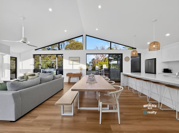 Bright and open living space seamlessly connects dining and kitchen areas, featuring large windows with natural light.