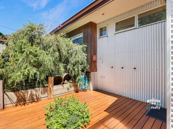 Bright and inviting outdoor space featuring a wooden deck, unique architectural details, and lush greenery.
