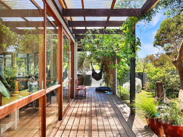 This inviting covered deck offers a perfect blend of indoor-outdoor living, surrounded by lush greenery.