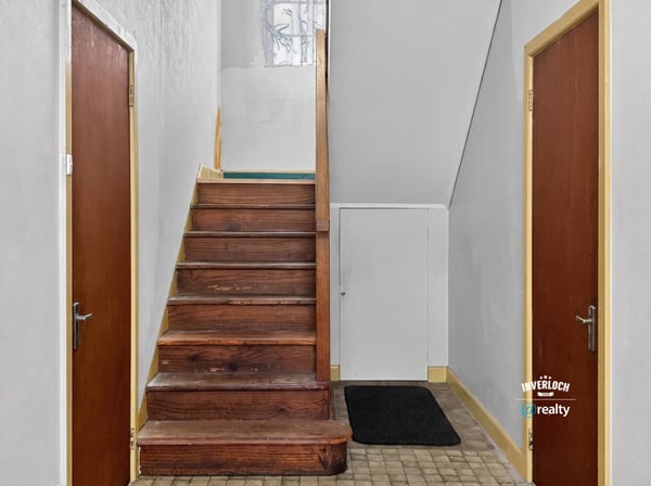 Bright entryway featuring a wooden staircase and dual access doors, perfect for welcoming guests.