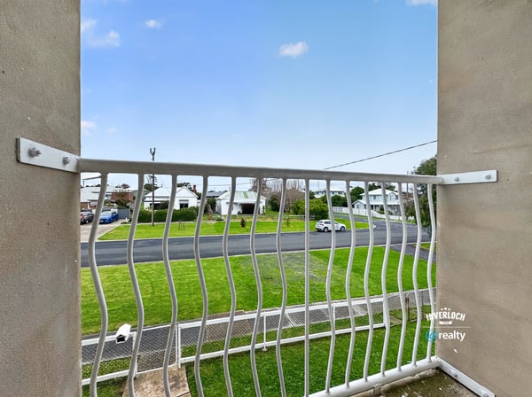 Enjoy a peaceful balcony view overlooking a quiet street surrounded by greenery and residential homes.