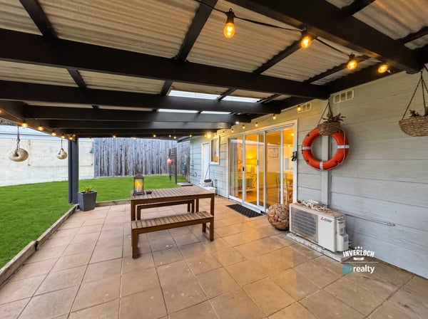 Spacious outdoor patio with hanging lights and lawn, perfect for gatherings and relaxed evenings.