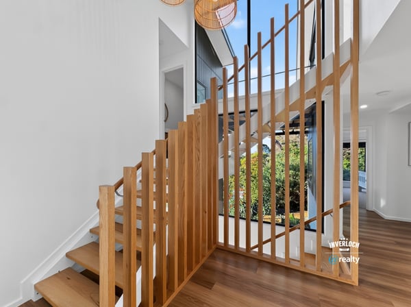 Modern staircase with striking wooden accents, leading to a bright, open living space filled with natural light.