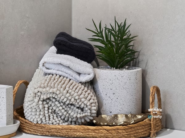 This inviting bathroom features neatly arranged towels and a contemporary plant in a chic basket.
