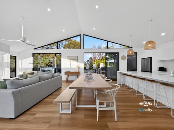 Bright and open living space seamlessly connects dining and kitchen areas, featuring large windows with natural light.