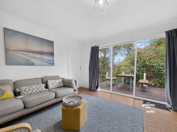 Bright living area featuring large sliding doors that open to a private outdoor deck surrounded by greenery.