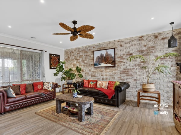 Spacious living area featuring a unique brick wall, rich colors, and a tropical-inspired ceiling fan.