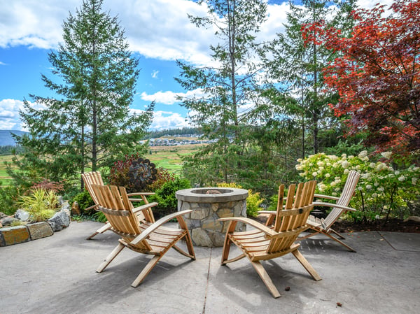 Cozy outdoor patio featuring a stone fire pit, next to the pool fountain, surrounded by greenery, and with stunning panoramic views.