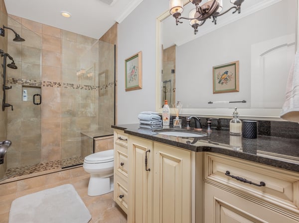 This modern ensuite bathroom features a spacious walk-in shower, granite countertops, and a sophisticated layout.