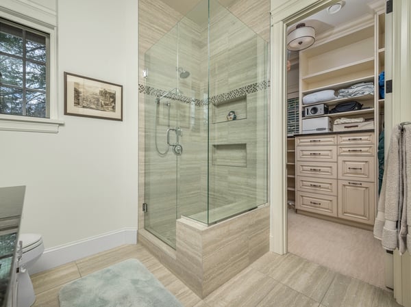 Modern bathroom featuring a spacious glass shower, neutral tones, and ample storage in a nearby large closet with extensive cabinetry.