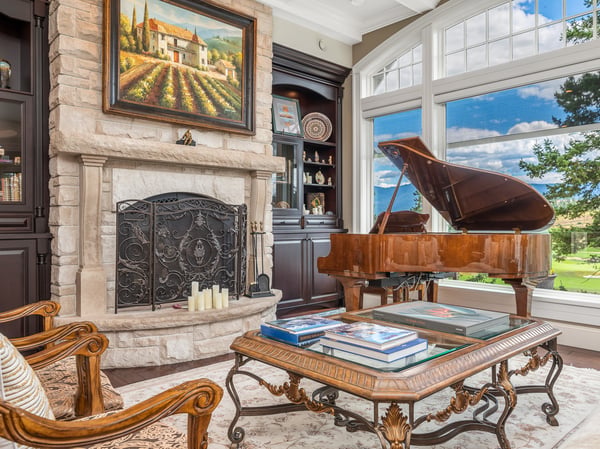 This inviting living space features a grand piano, stone fireplace, and picturesque window views of the outdoors.