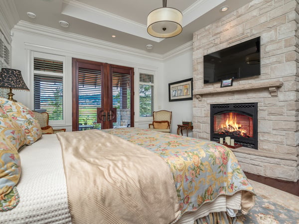 Primary bedroom featuring a fireplace, comfortable seating, and access to an outdoor balcony with views through French doors.