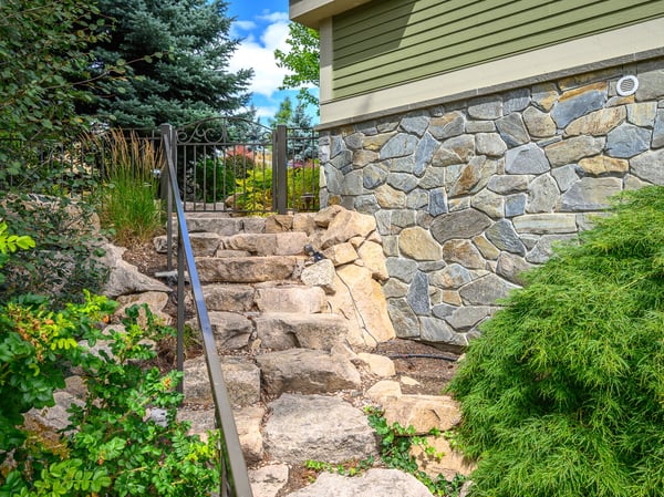 Discover a beautifully landscaped entryway featuring natural stone steps and lush greenery, inviting you home.
