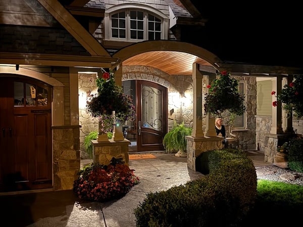 This welcoming home features a beautifully lit entrance, showcasing exquisite stonework and vibrant landscaping.