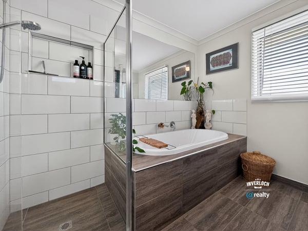 Modern bathroom featuring a spacious tub, glass shower, and organized space with natural light.