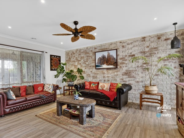 Spacious living area featuring a unique brick wall, rich colors, and a tropical-inspired ceiling fan.