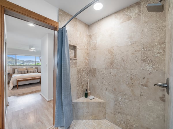 Bright and spacious bathroom with natural stone finishes, featuring a walk-in shower and scenic views.