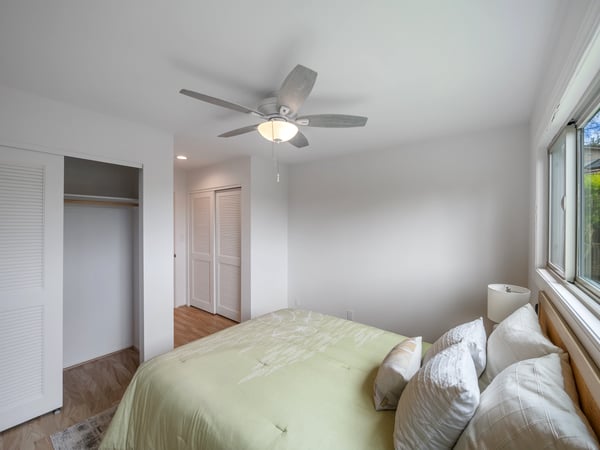 Bright and airy bedroom featuring a ceiling fan, ample closet space, and large windows for natural light.