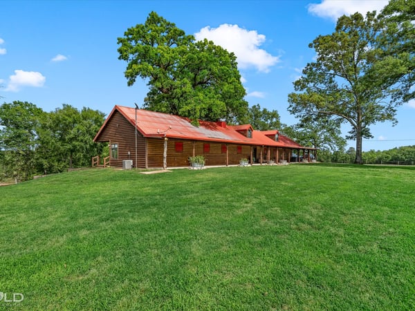 Spacious countryside home with a welcoming porch, surrounded by lush greenery and open skies.
