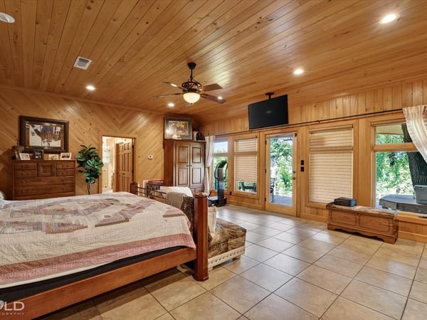 Spacious master bedroom featuring wood accents, large windows, and direct access to outdoor greenery.